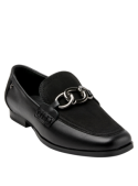 Detalle del zapato de cuero negro mostrando costuras definidas y cadena metálica que aporta un toque moderno.